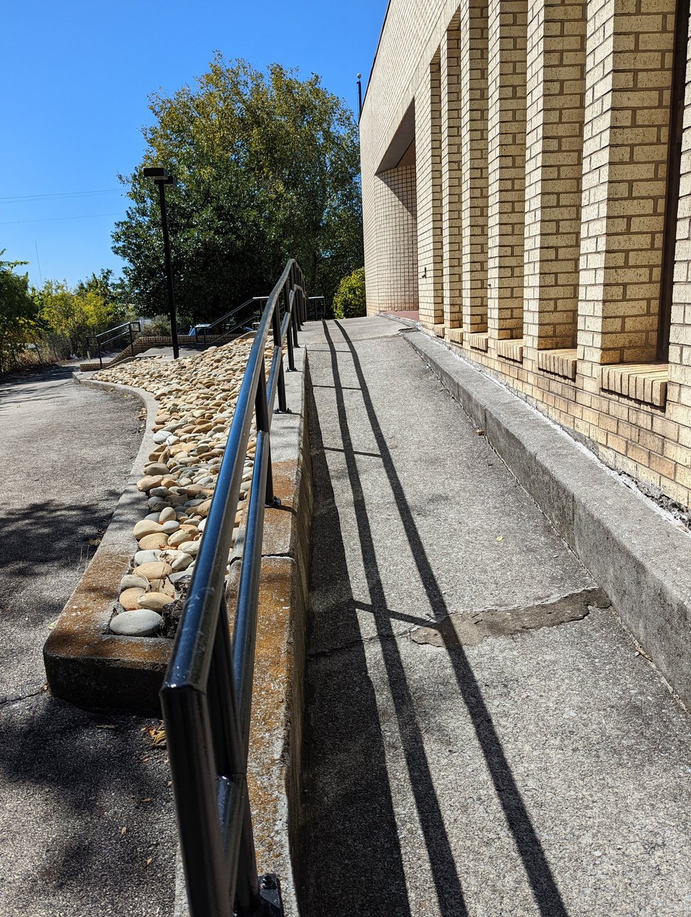 A sidewalk ramp with a metal handrail running along the brick building.