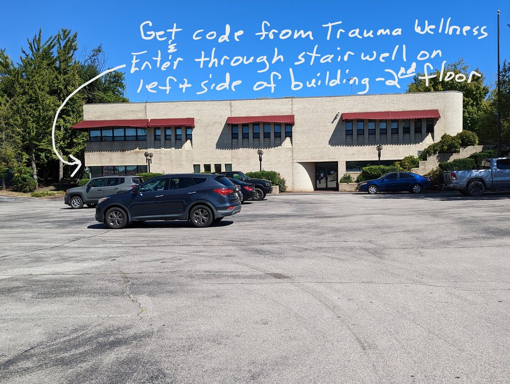 The front of the white brick building with red awnings, seen from the parking lot. A handwritten arrow points to the left side of the building.