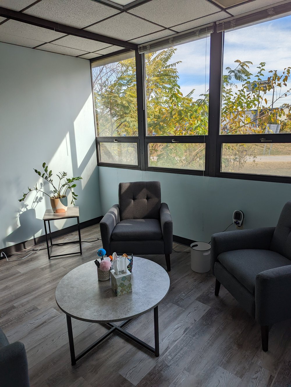 A waiting area with two gray armchairs, a small table and large windows.
