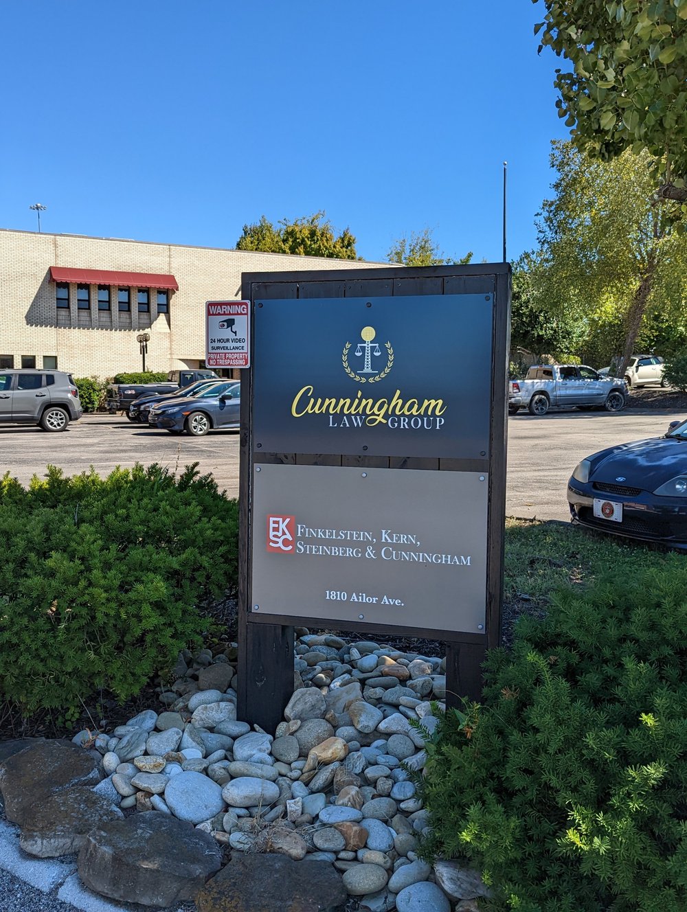 The building sign for Cunningham Law Group and Finkelstein, Kern, Steinberg and Cunningham, with cars and trees behind it.